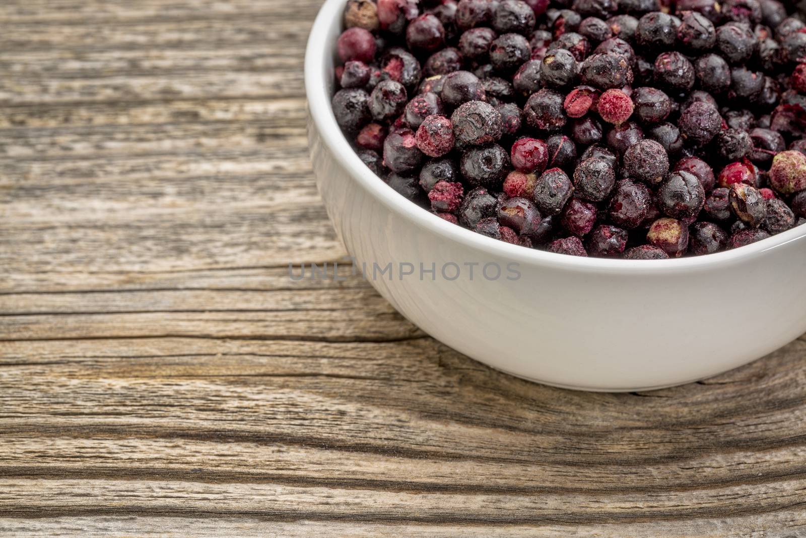 freeze dried elderberries in white, ceramic bowl against grained wood