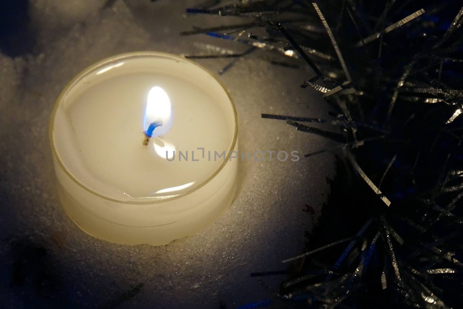  Candle in the snow and tinsel in the blue twilight                                   