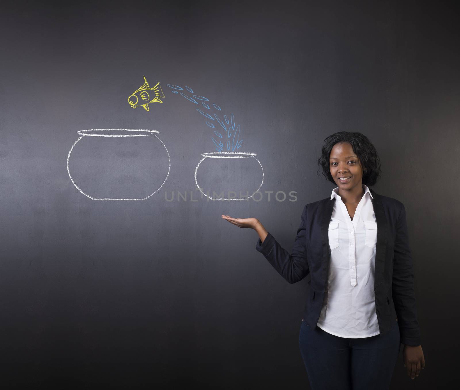 South African or African American woman teacher or student holding her hand up with a fish jumping from a small bowl to a big bowl on a blackboard background