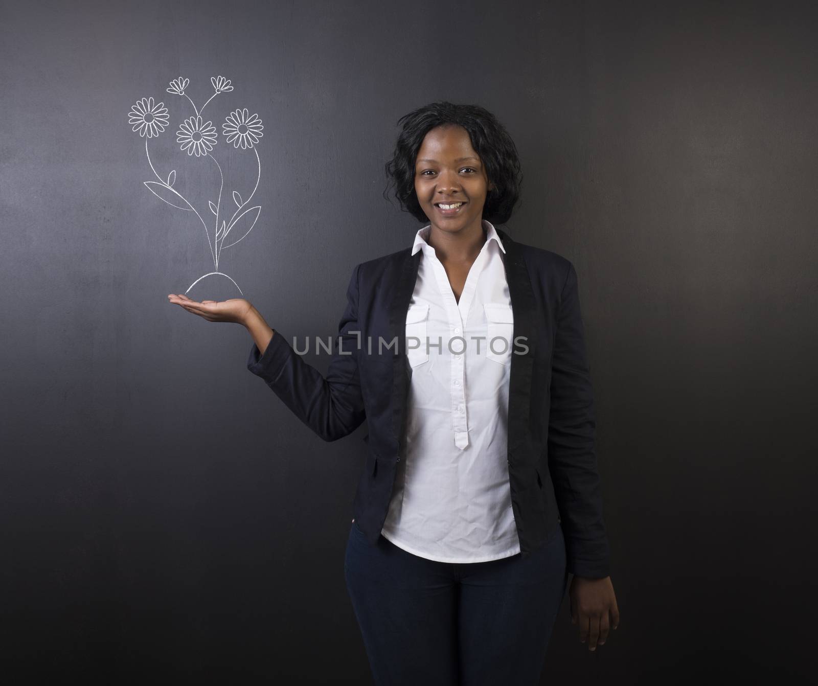 South African or African American woman teacher or student holding her hand out standing against a blackboard background holding chalk growing flowers