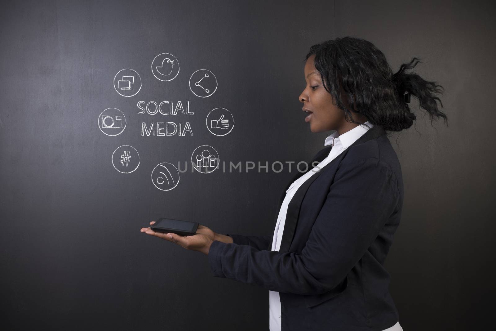 South African or African American woman teacher or student excited holding a tablet computer against a blackboard background with a social media chalk concept