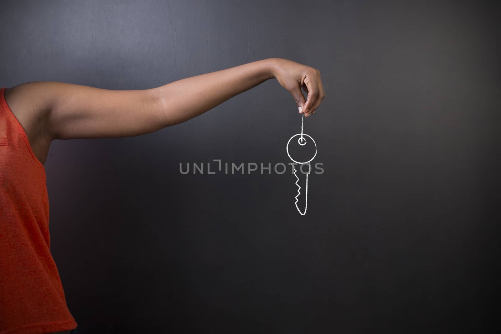 South African or African American woman teacher or student holding her hand out holding a chalk key standing against a blackboard background