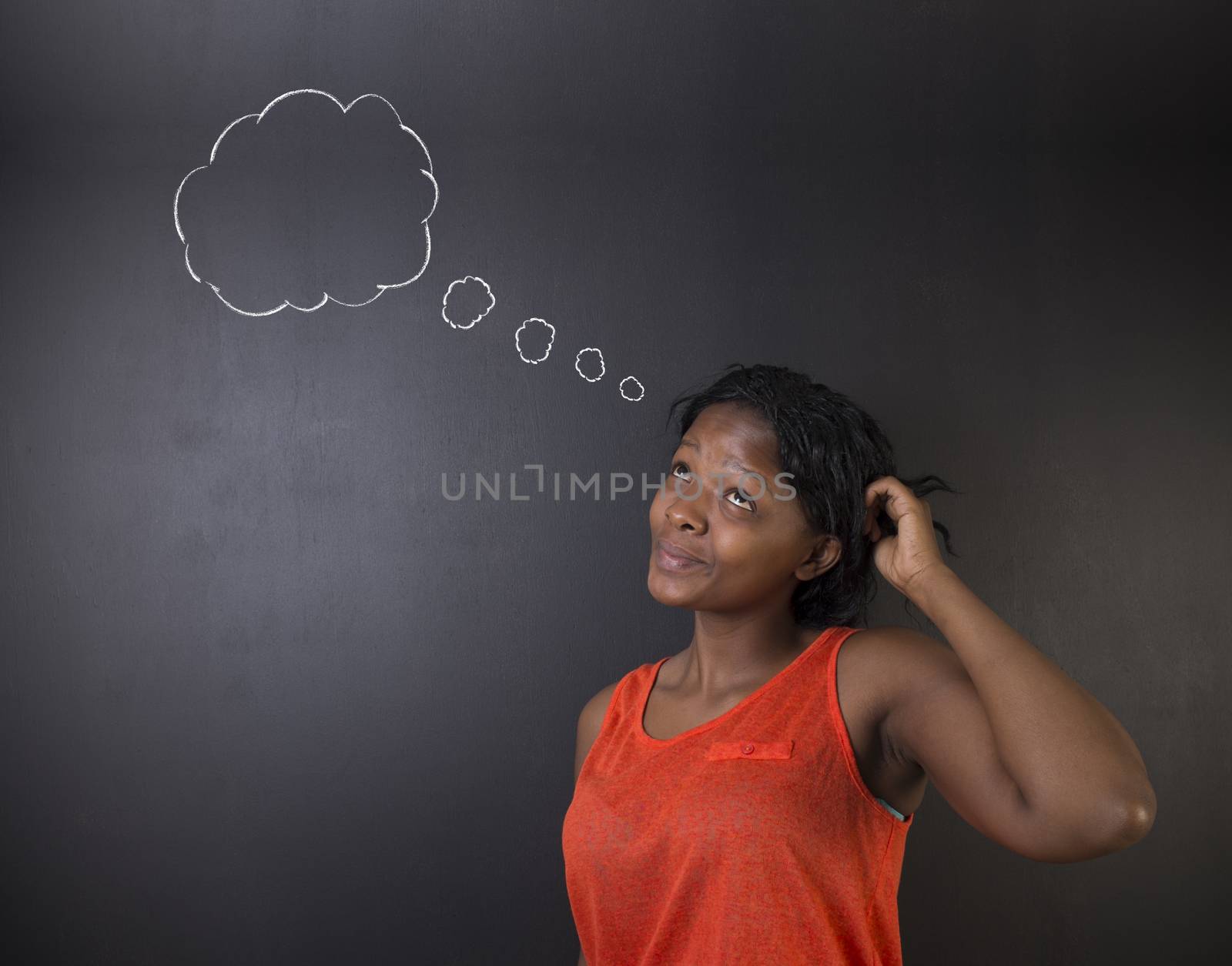 South African or African American woman teacher or student thinking, scratching her head standing against a blackboard background with chalk thought clouds