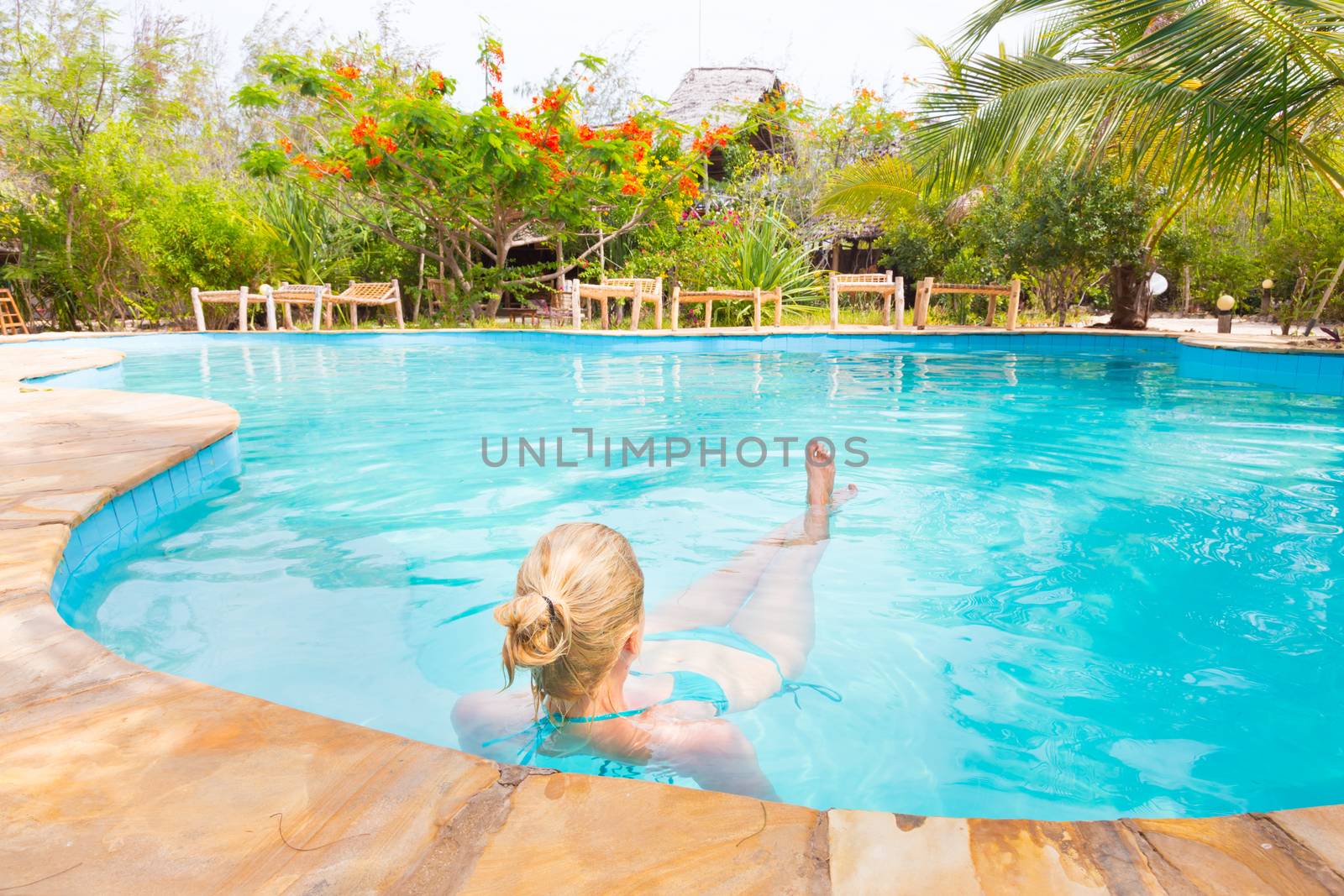 Beautiful Caucasian woman floating in turquoise blue swimming pool.