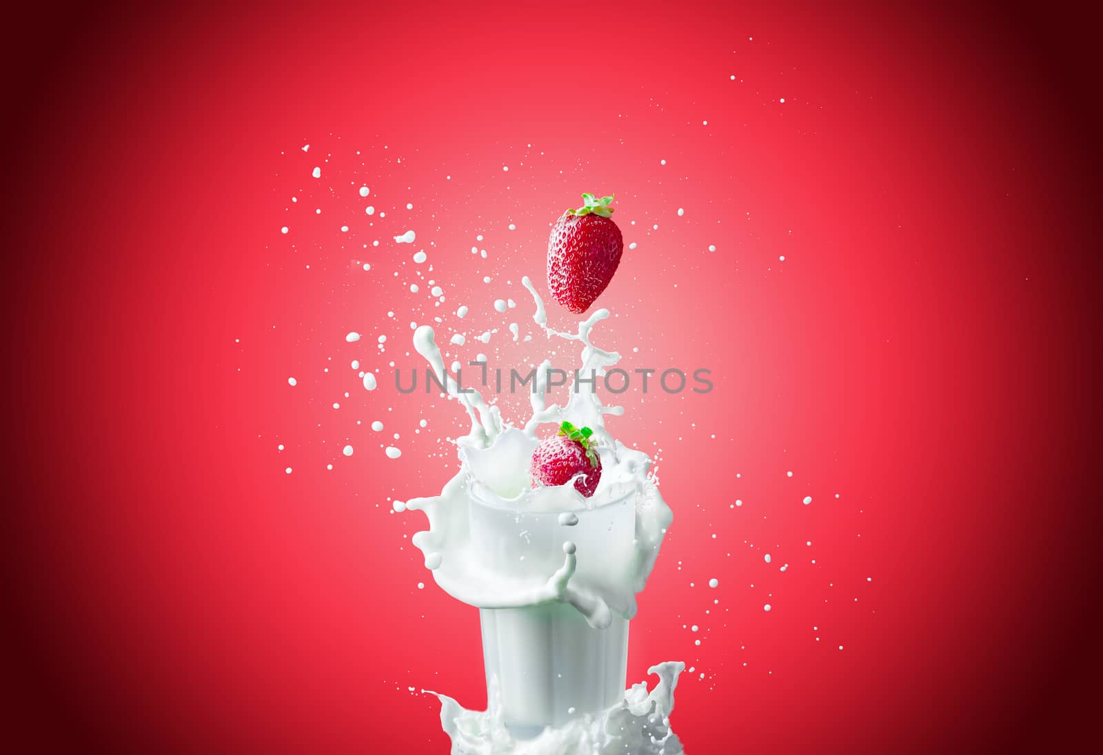 View of nice fresh red strawberry falling down in to the glass milk making a big splash on a red background