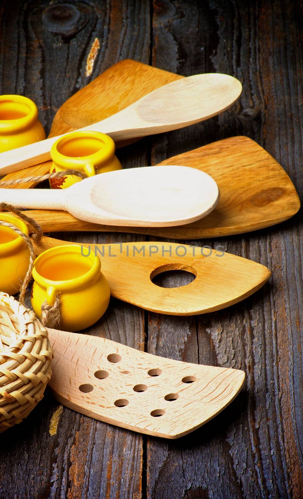 Heap of Kitchen Utensils with Wooden Spoons, Spatula, Wicker Bowl and Small Pots closeup on Rustic Wooden background