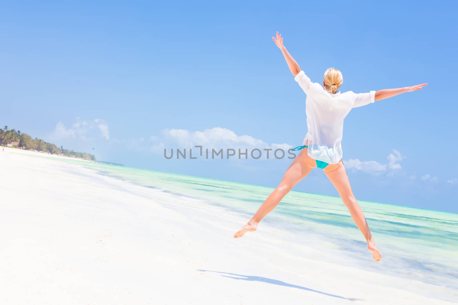 Beautiful Girl Jumping on Beach. Vacation Concept Woman enjoying, relaxing joyfully in summer. Beautiful caucasian model wearing white tunic jumping on picture perfect Paje beach, Zanzibar, Tanzania.