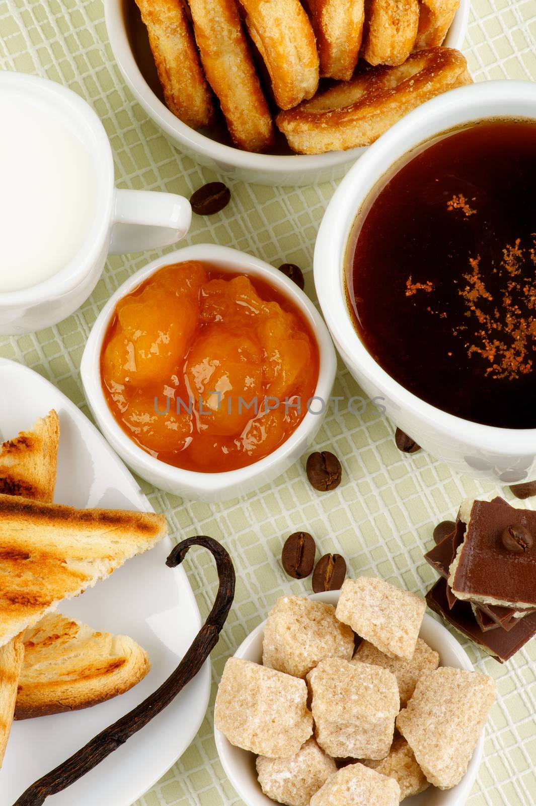 Tasty Breakfast with Coffee Cup, Chocolate, Sugar Cubes, Toasts, Apricot Jam, Milk and Puff Pastry on Checkered background. Top View