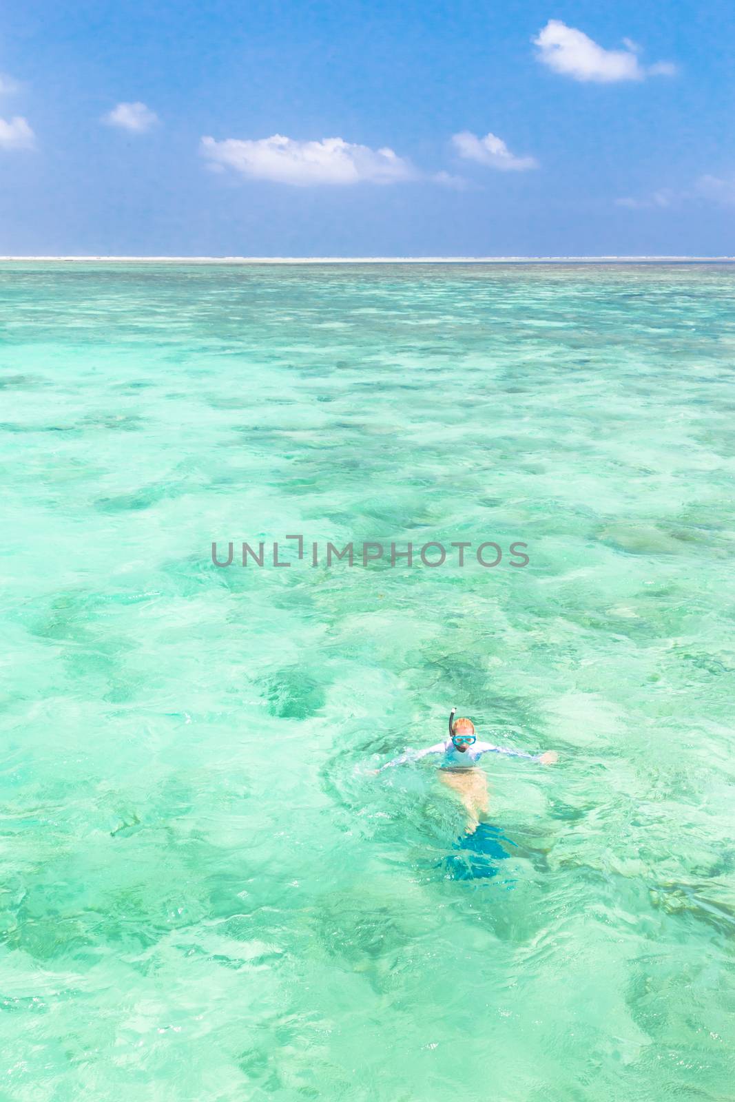 Young woman snorkeling in clear shallow sea of tropical lagoon with turquoise blue water and coral reef,  near exotic island. Mnemba island, Zanzibar, Tanzania.