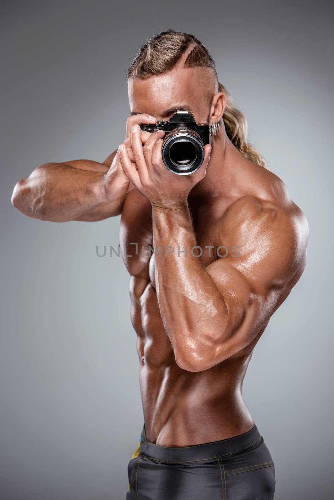Attractive male body builder as photograph holding a camera on gray background
