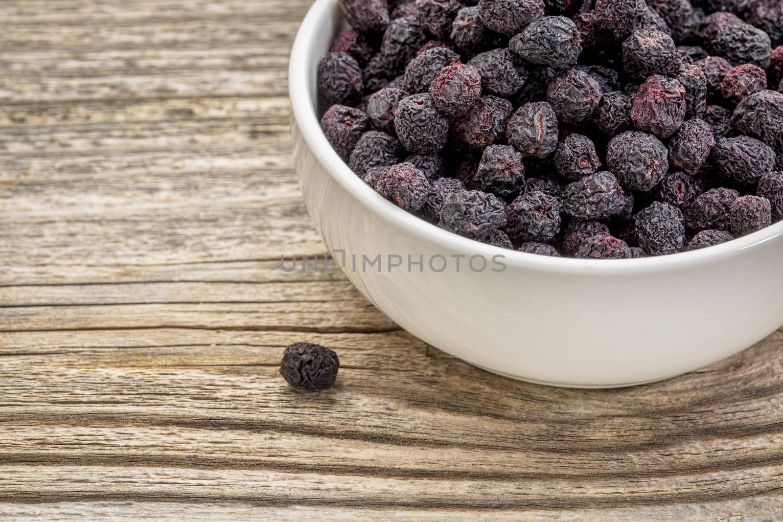 Dried chokeberry (aronia berry) in a small, ceramic bowl against grained wood