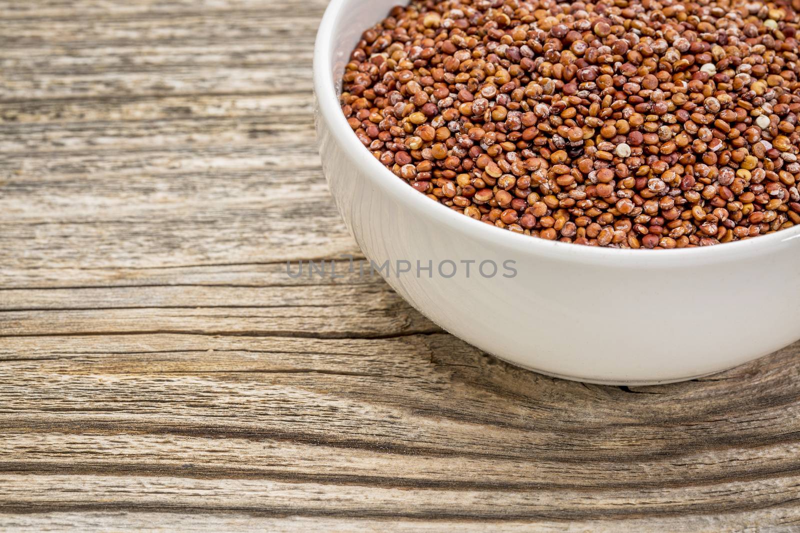 gluten free, red quinoa grain in a small, ceramic bowl against grained wood