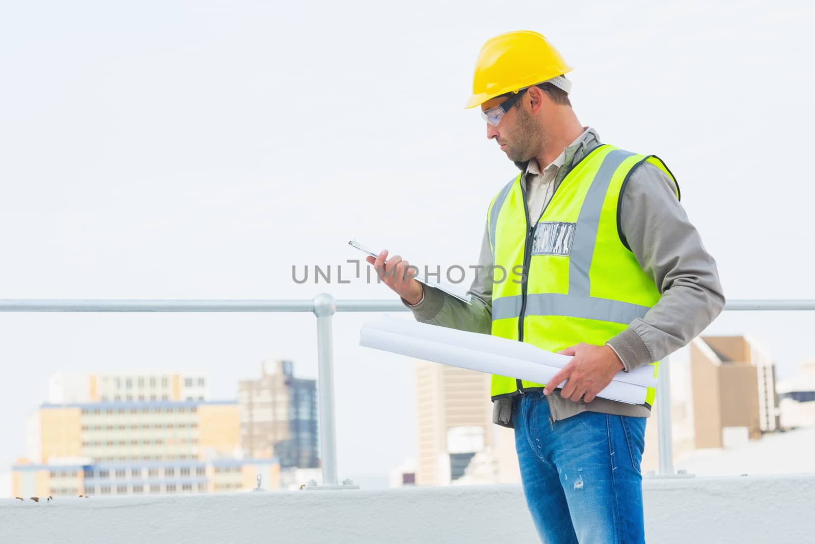 Male architect with blueprints reading clipboard outdoors