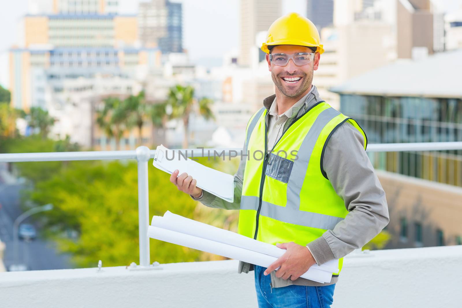 Portrait of smiling male architect with blueprints and clipboard outdoors