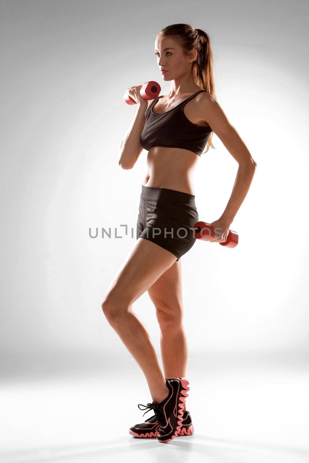 Sporty woman doing aerobic exercise with red dumbbells on grey background