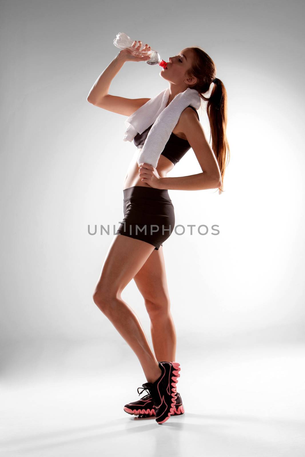 Sporty woman resting and drinking water on gray background