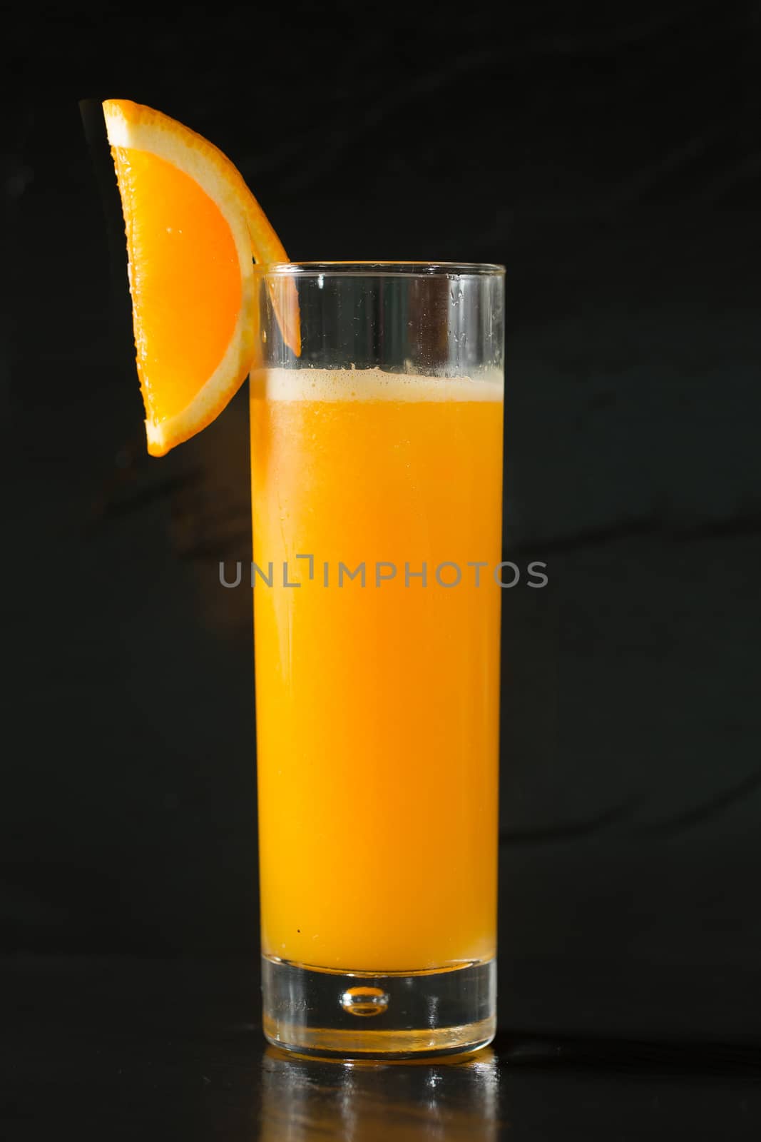 Glass of freshly pressed orange juice with sliced orange on black background
