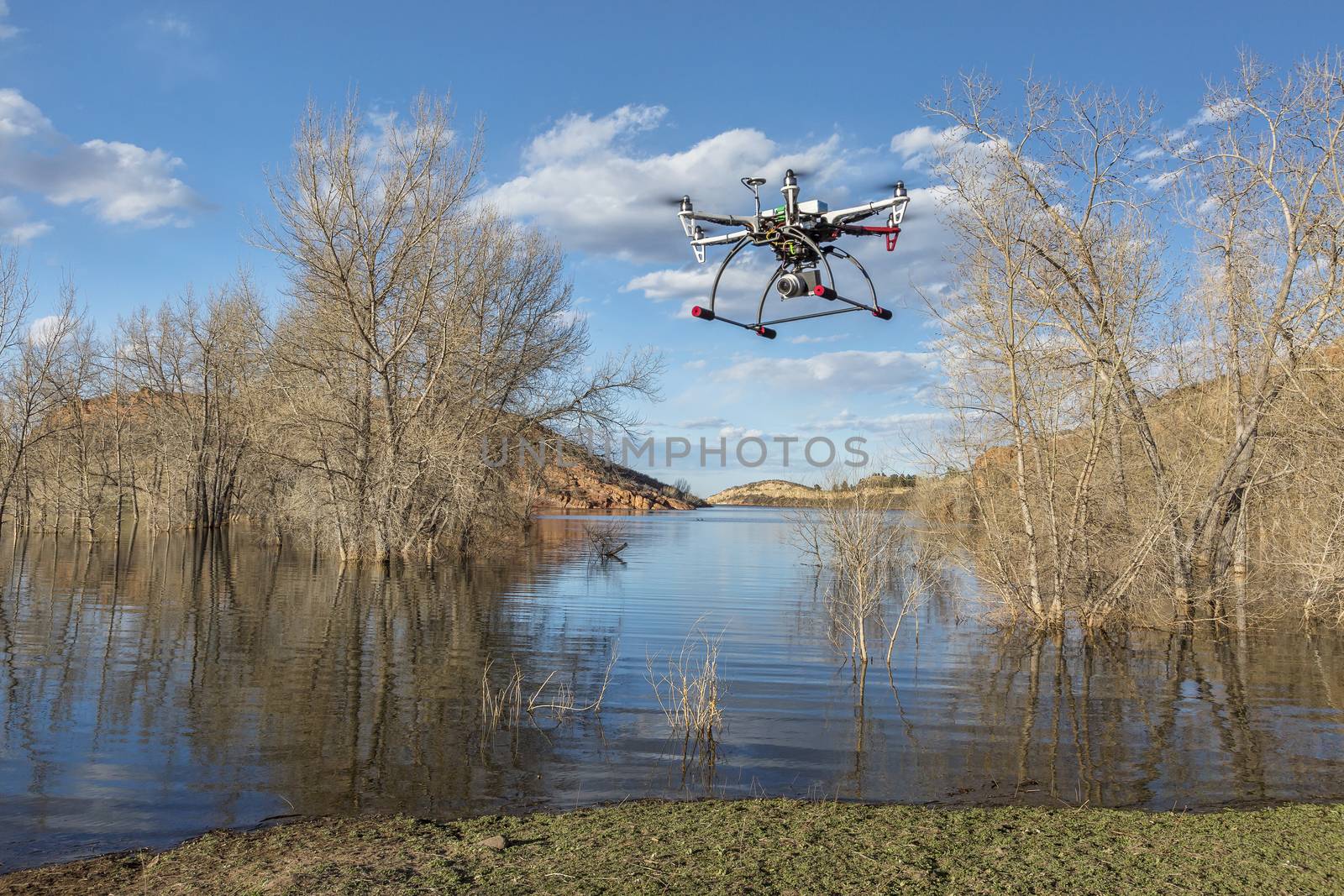 hexacopter drone flying over lake by PixelsAway