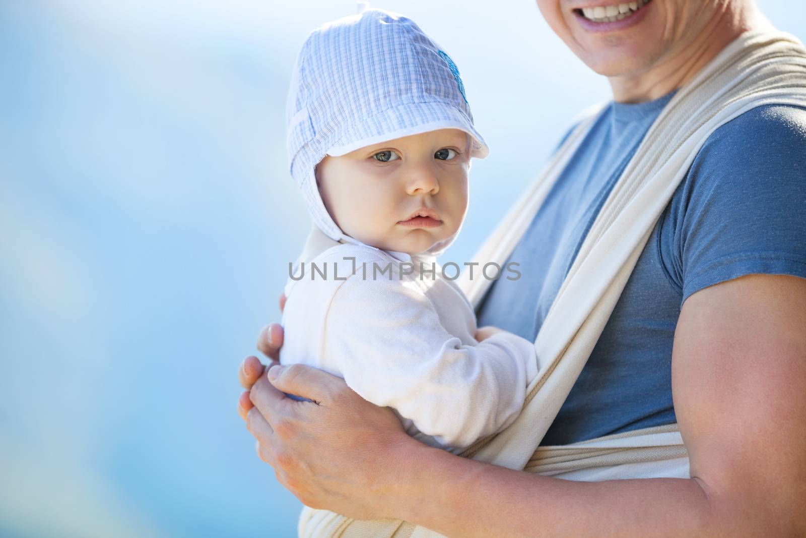 Cute toddler boy in sling, father carrying son outdoors