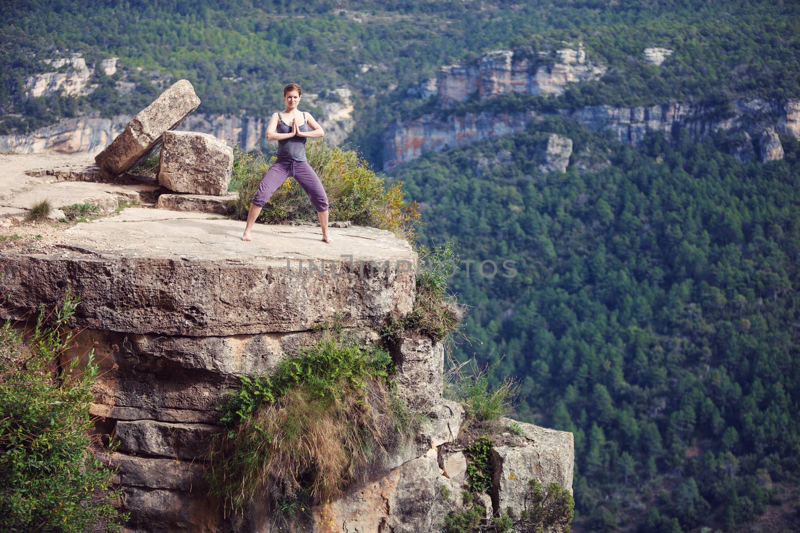 Young woman standing in yoga pose on top of cliff by photobac