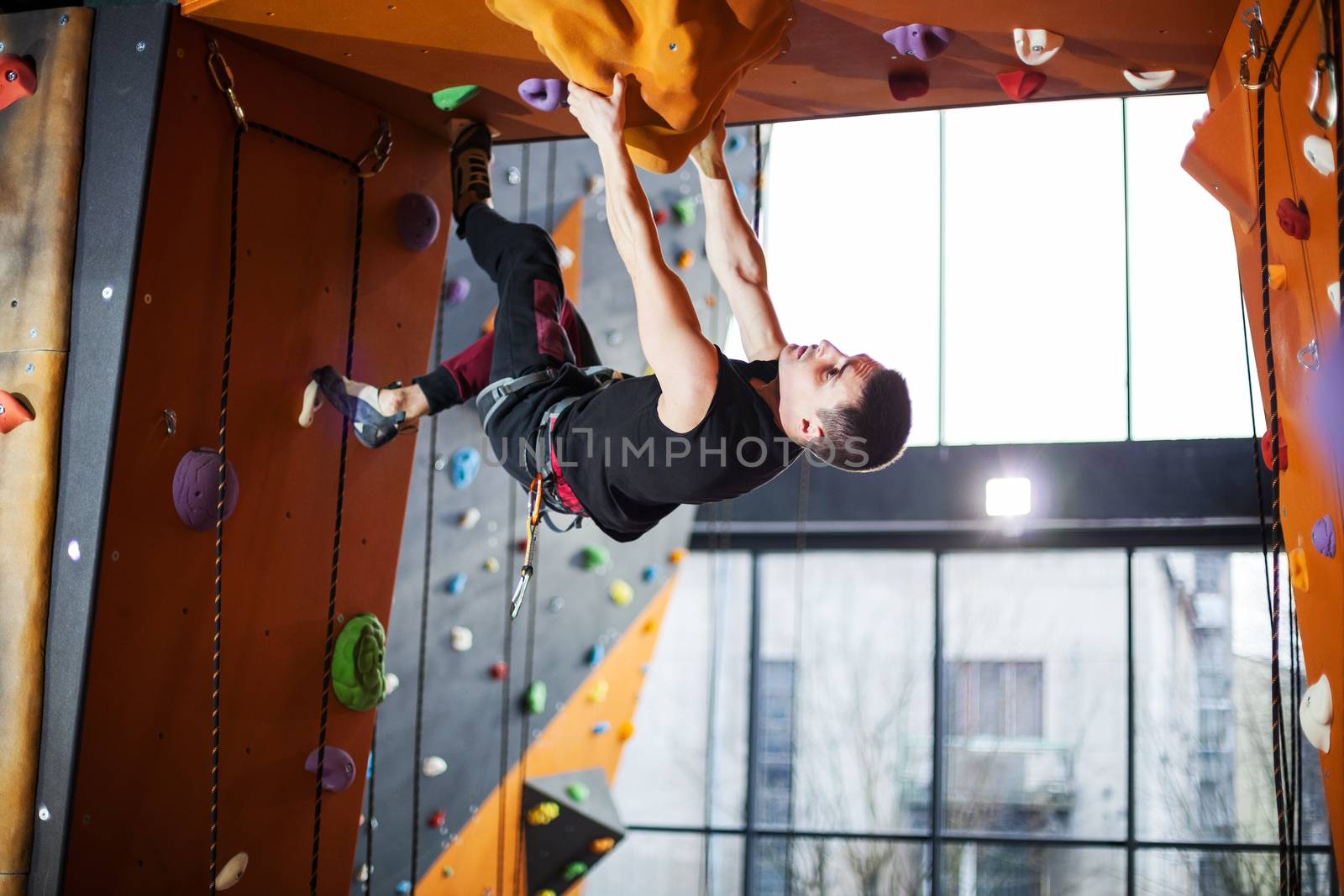 Man practicing top rope climbing in climbing gym by photobac
