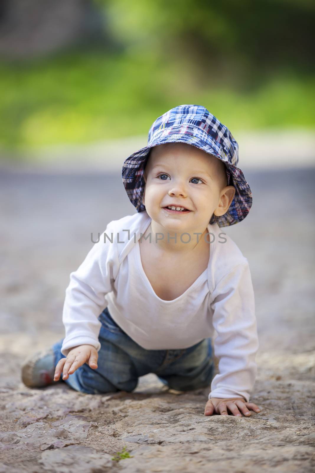 Cute little boy looking up and smiling while crawling on stone paved sidewalk