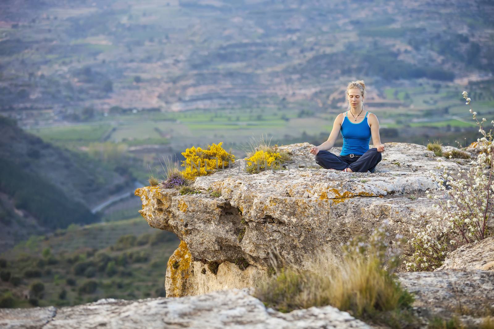 Young woman sitting on a rock in asana position by photobac