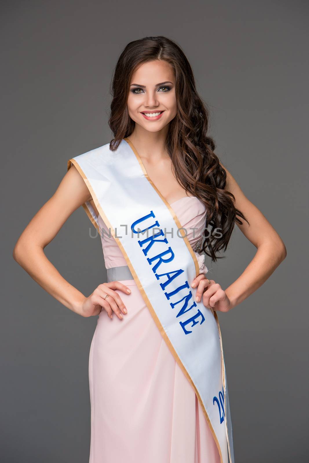 Sexy young brunette woman with her hair posing in a long pink dress in studio on gray background 