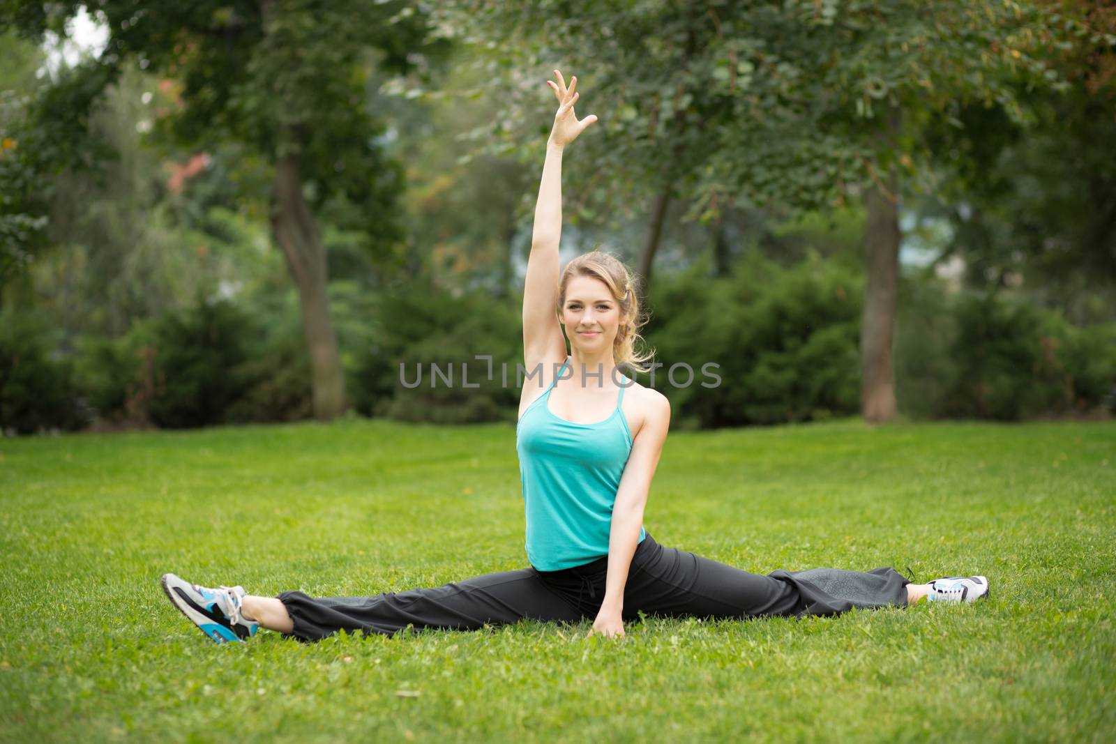 Beautiful young woman doing stretching exercises in the park. Green grass  background 