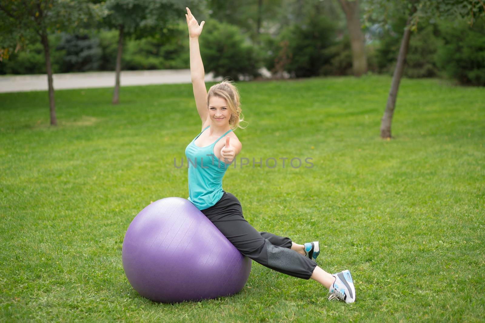 Young happy woman with fitness ball, outdoor. Green grass background 