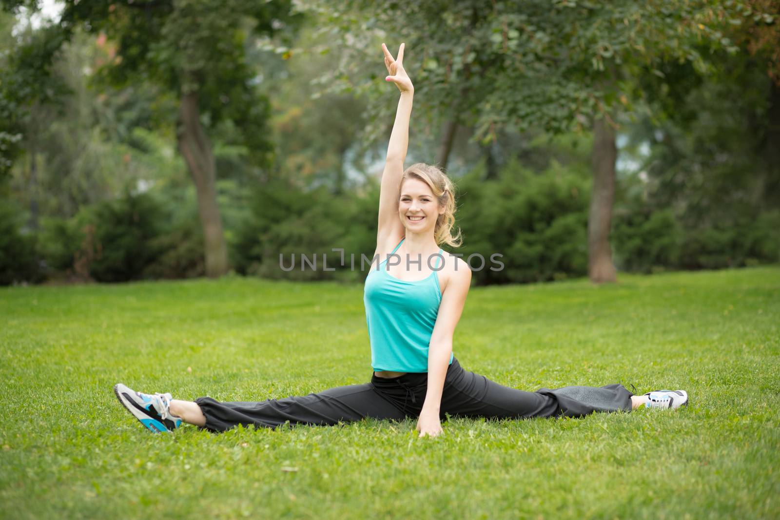 Beautiful young woman doing stretching exercises in the park. Green grass  background 