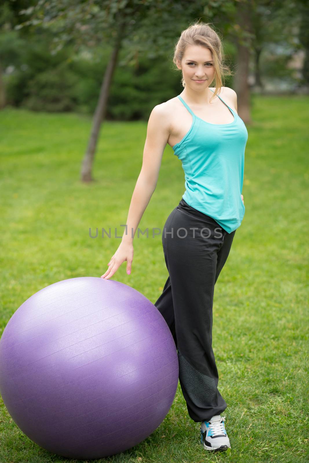 Young happy woman with fitness ball, outdoor. Green grass background 