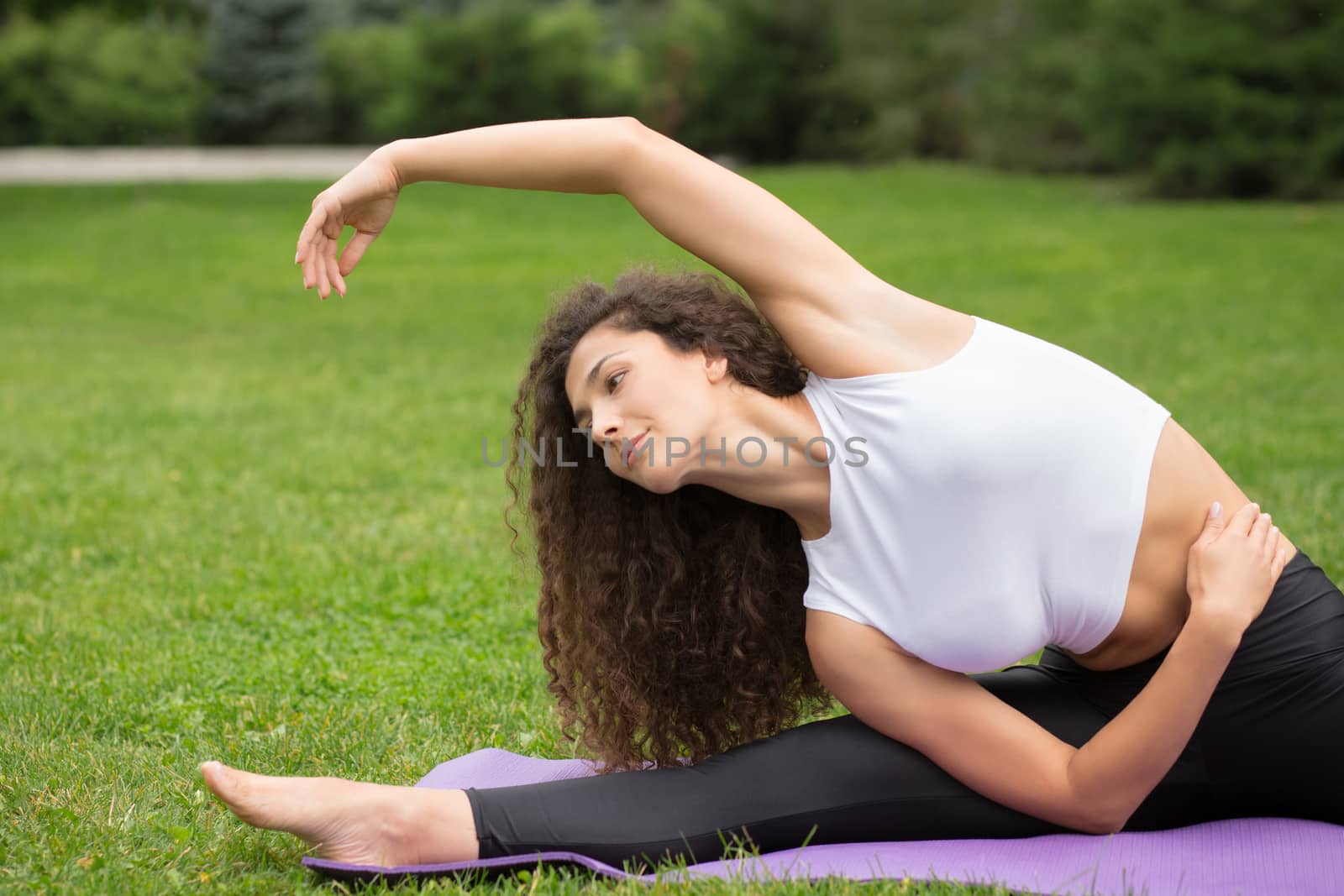 Pretty woman doing yoga exercises in outdoor park, green grass background 
