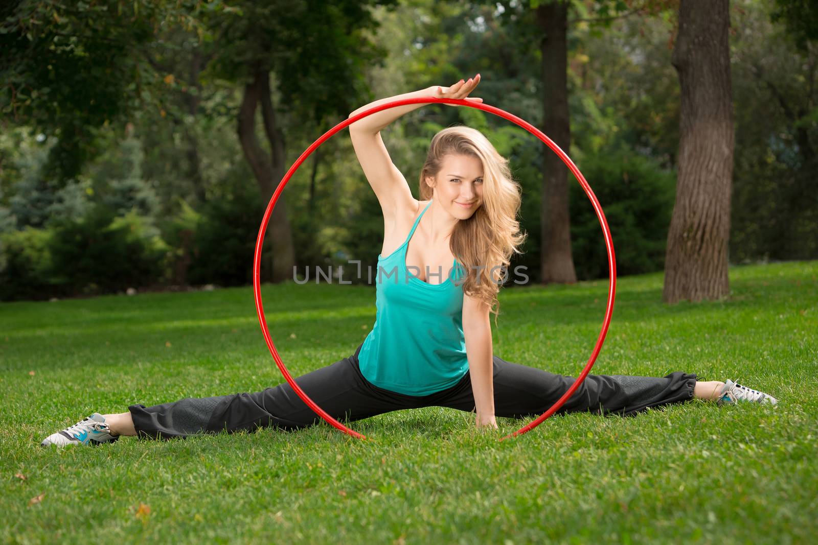 Young female athlete holding a hula hoop in the park. Green grass