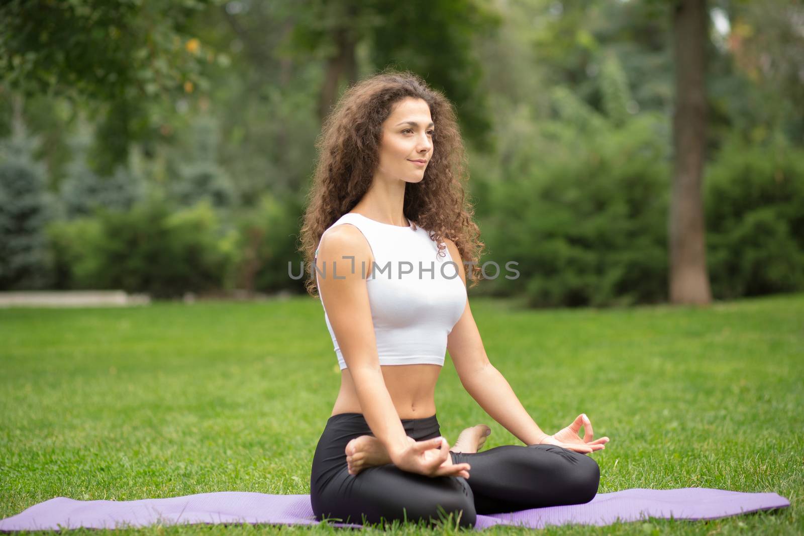 Pretty woman doing yoga meditation in the lotus position. Green grass background 