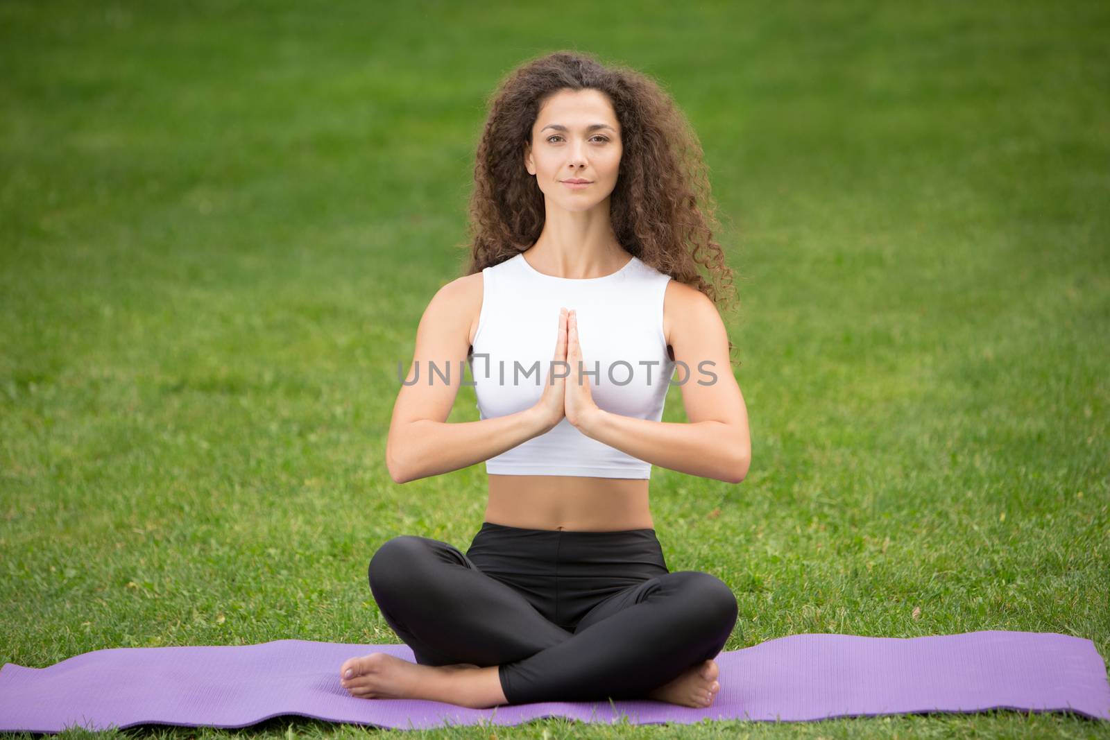 Pretty woman doing yoga meditation in the lotus position. Green grass background 