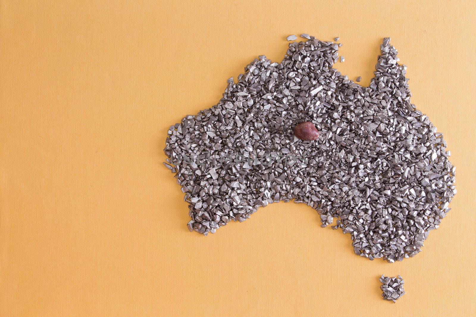 Conceptual map outline of Australia and Tasmania formed from an arrangement of silvery stone chips and fragments on a yellow textile background with copyspace