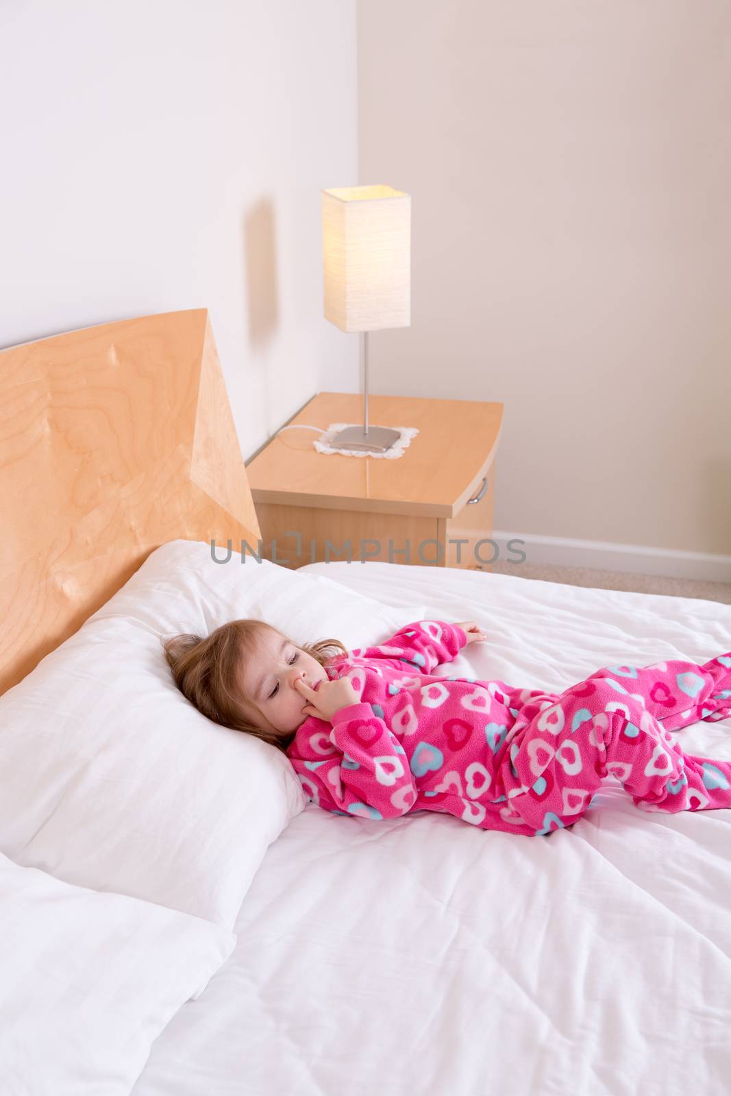 Small girl in pink pajamas lying resting on a bed by coskun