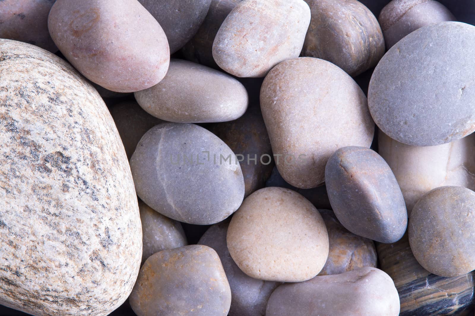 Background texture of smooth oceanic stones eroded by the force of the tides and currents to a rounded form before being deposited on the seashore