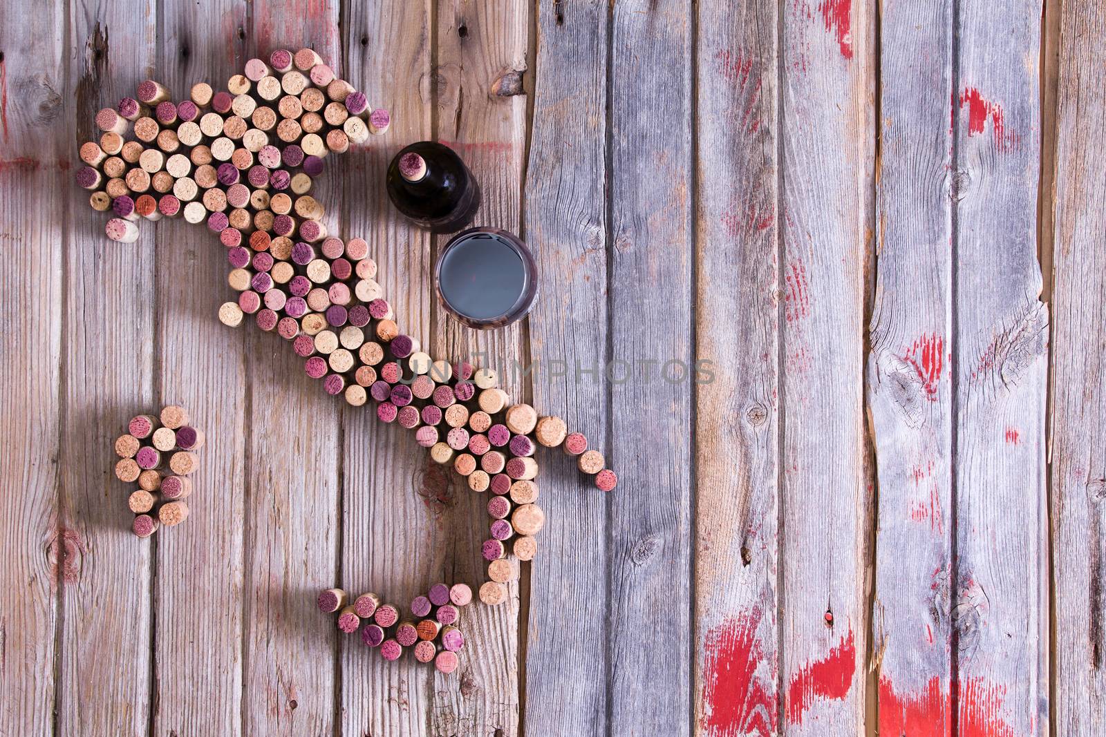 Artistic conceptual map of Italy, Sardinia and Sicily made of old red and white wine bottle corks on an old rustic wooden table with a glass and bottle of red wine alongside