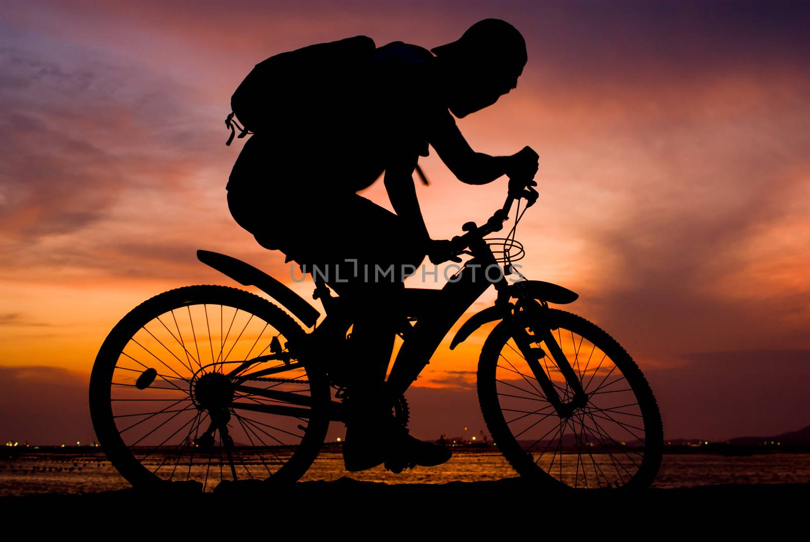 Silhouette of backpacker ride mountain bike on bridge beside sea with sunset sky background