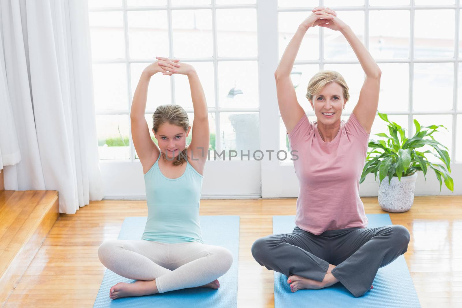 Mother and daughter doing yoga on fitness mat at home in living room 