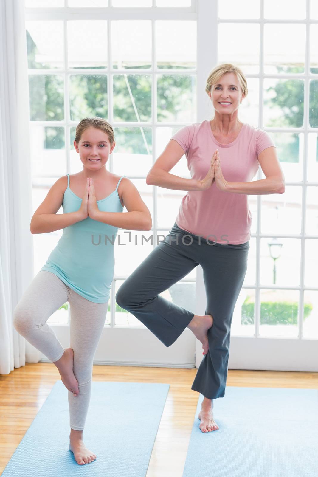 Mother and daughter doing yoga on fitness mat at home in living room 