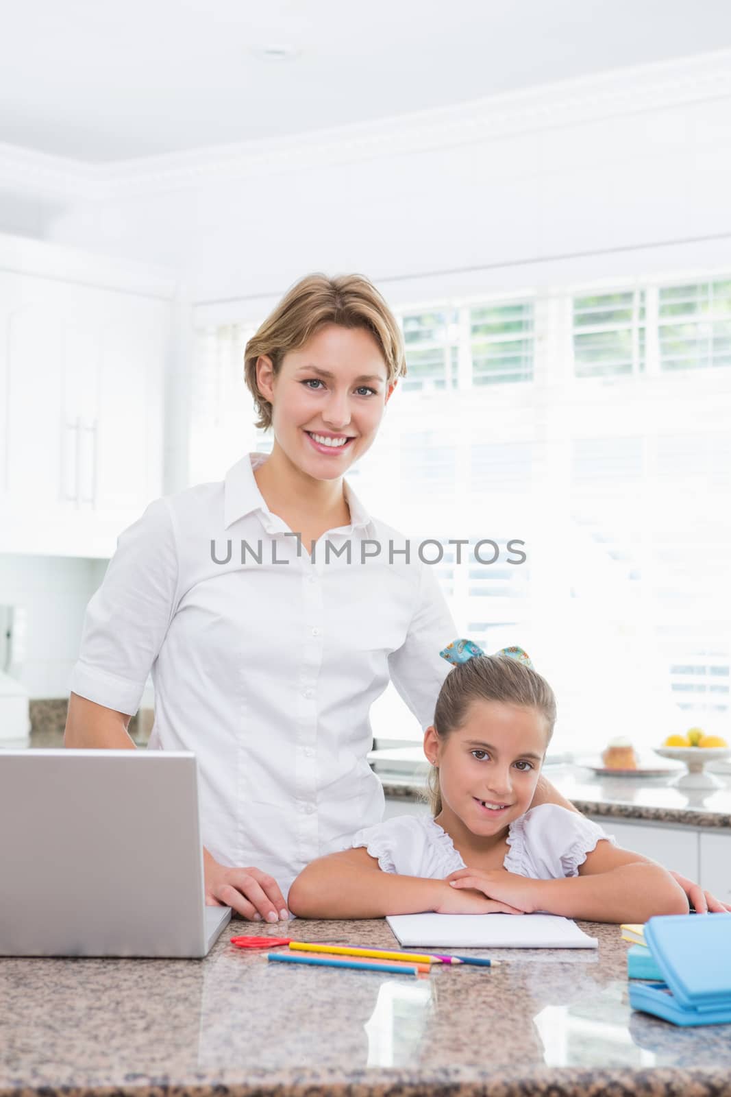 Little girl doing her homework with mother using laptop at home in kitchen