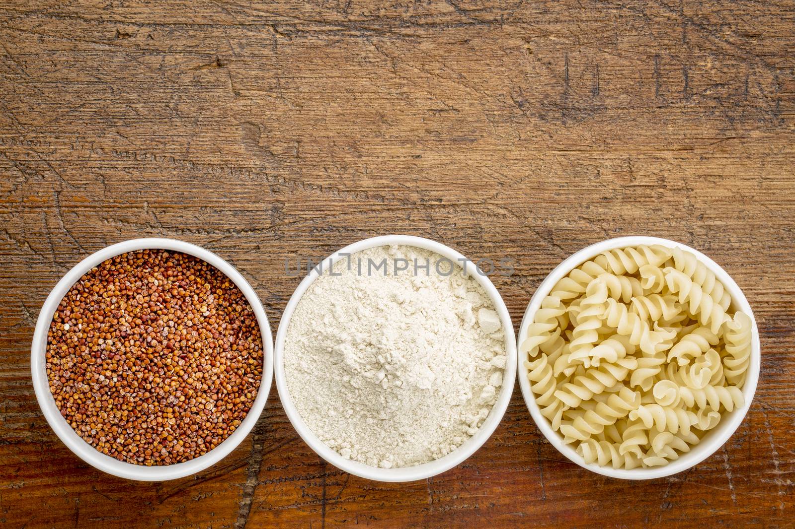 gluten free quinoa grain, flour and pasta - top view of small ceramic bowls against rustic wood with a copy space