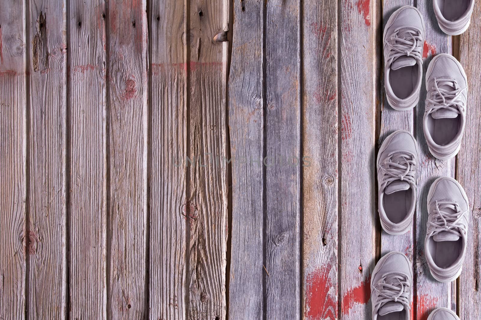 Shoe border with a double row of worn trainers or sneakers arranged as though walking on a textured hardwood background of old floorboards with wood grain, red paint remnants and copyspace