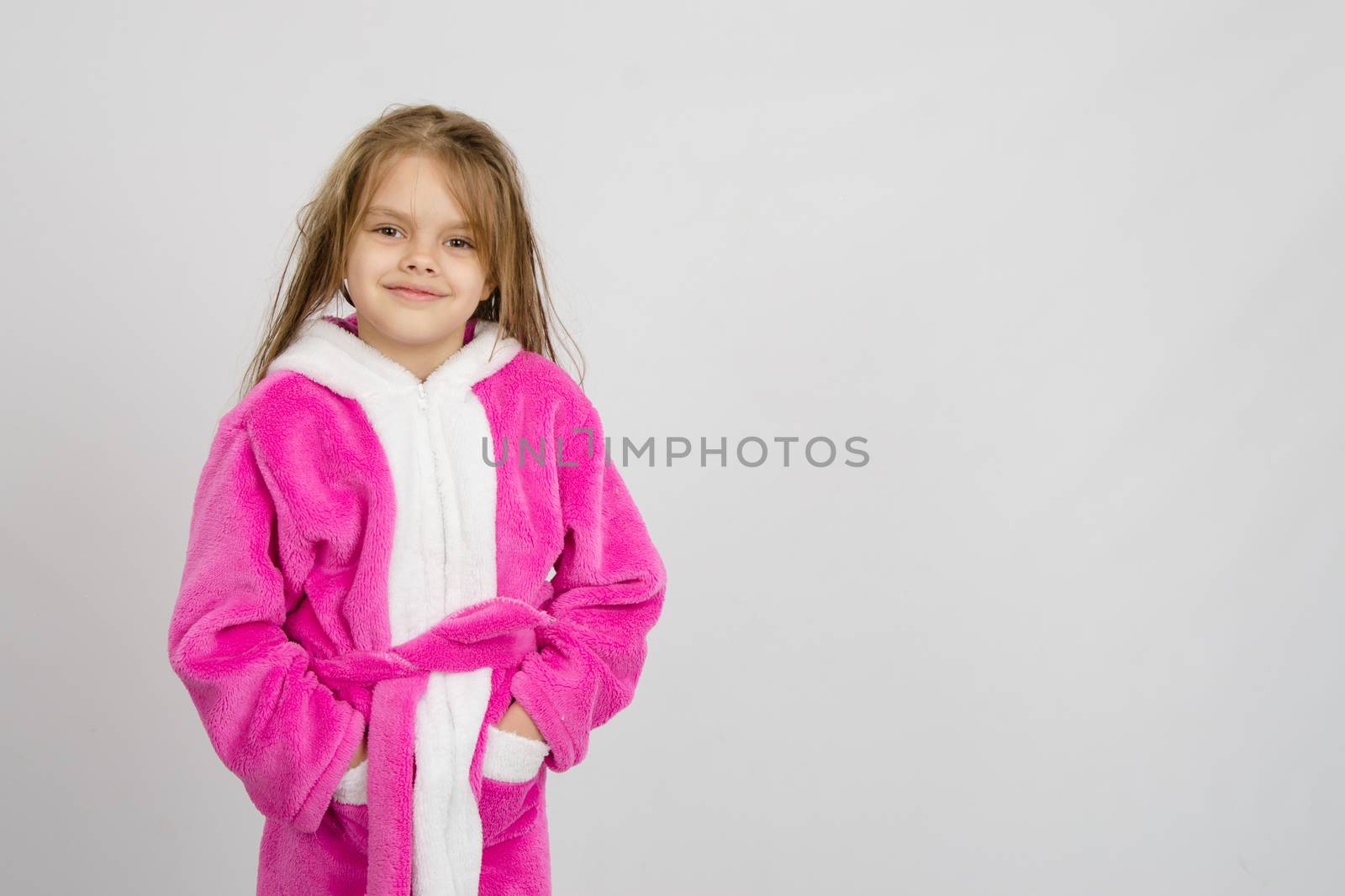 Six year old girl with wet hair in a bathrobe on a light background