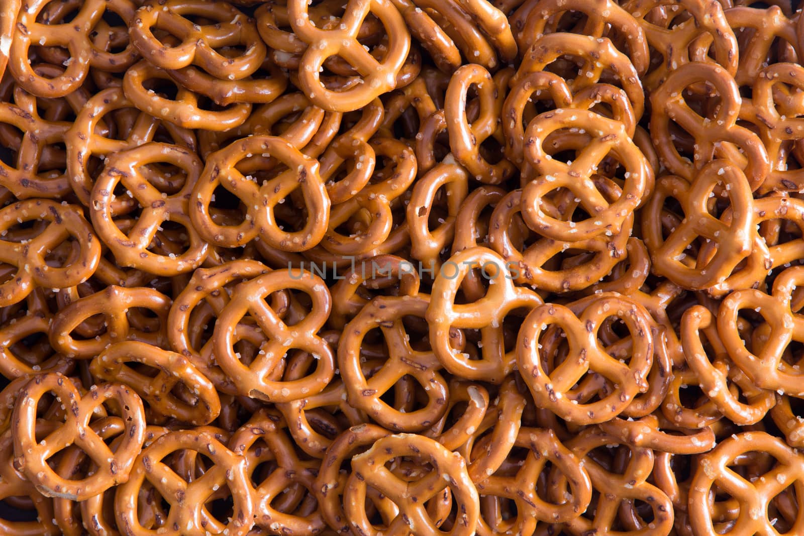Background texture of salted savory mini pretzels in the traditional looped knot shape in a random heap viewed full frame from overhead