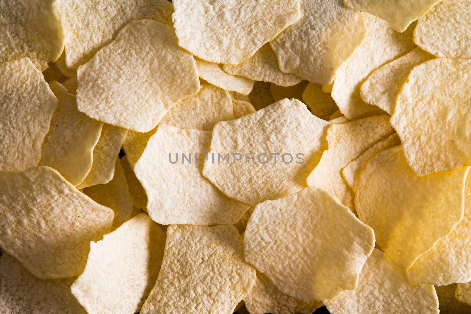 Close up background texture of golden oven baked potato chips for a tasty snack or appetizer viewed full frame from above