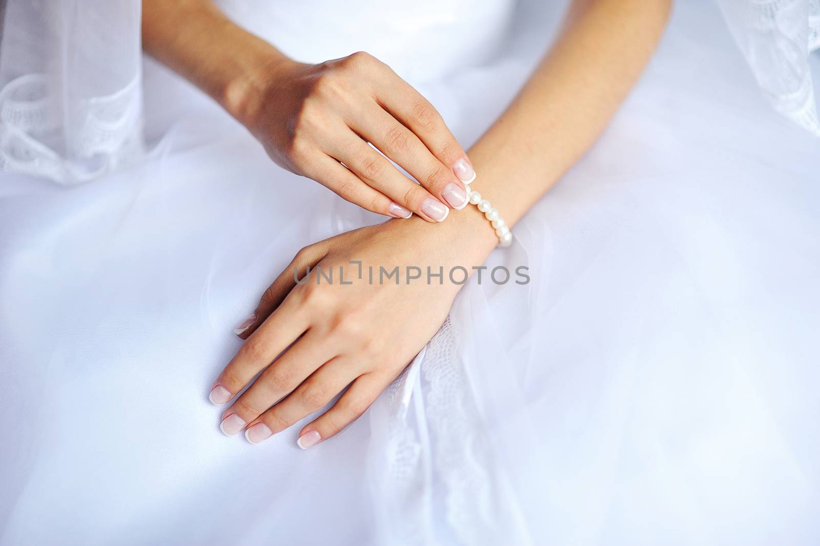 Bride's hands with manicure on the white wedding dress